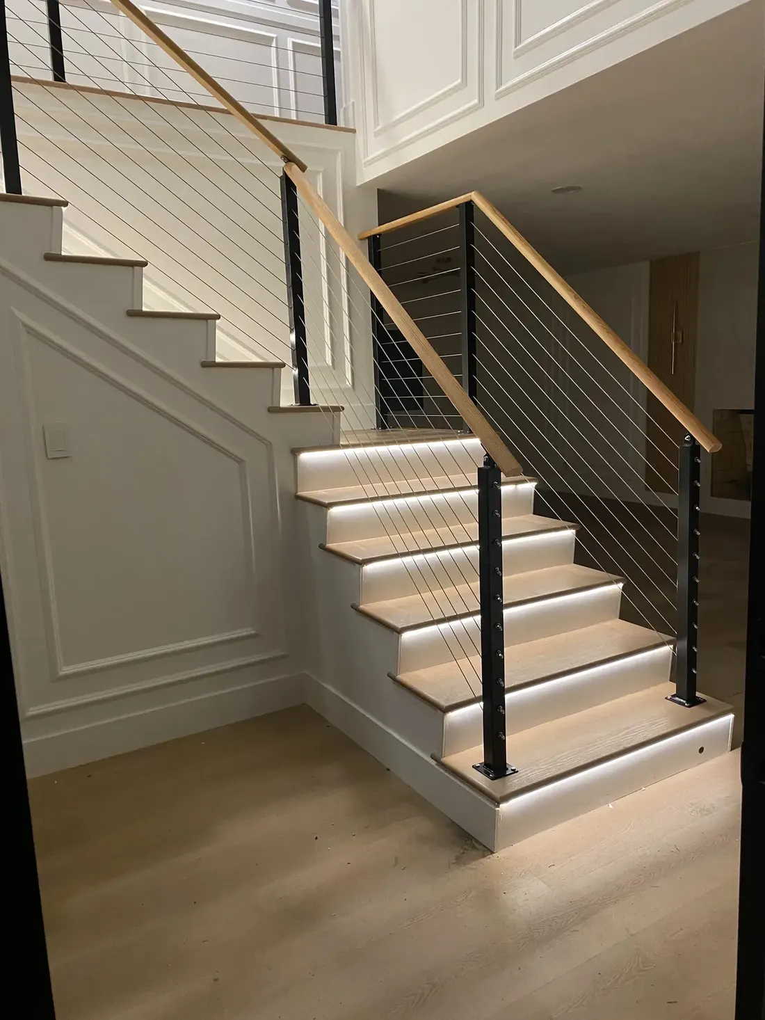Interior staircase with black posts, diagonal cable railing, and a natural-finish handrail